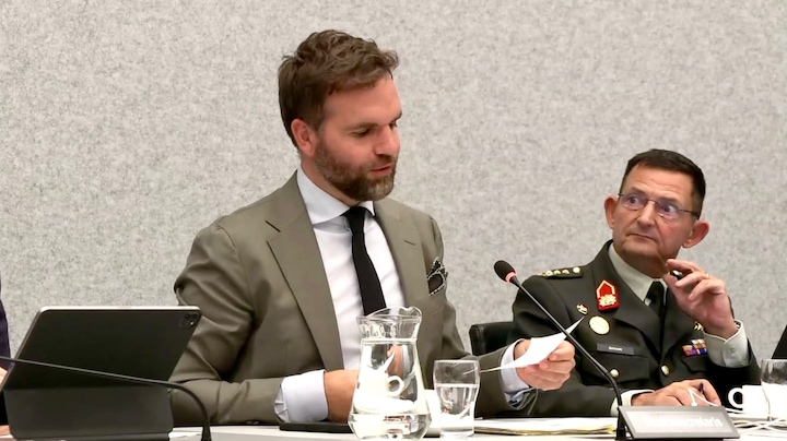 Staatssecretaris leest briefje van ambtenaar voor die hem tot snelheid maant